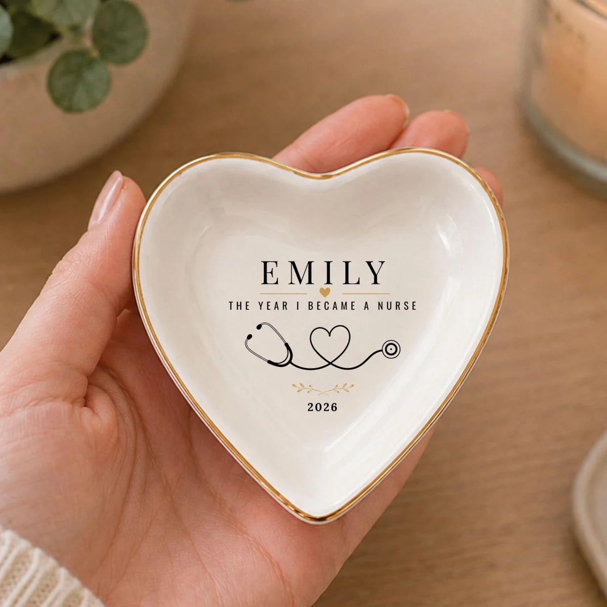 Hand holding a heart-shaped ceramic nurse ring dish with a name, stethoscope heart design and a year