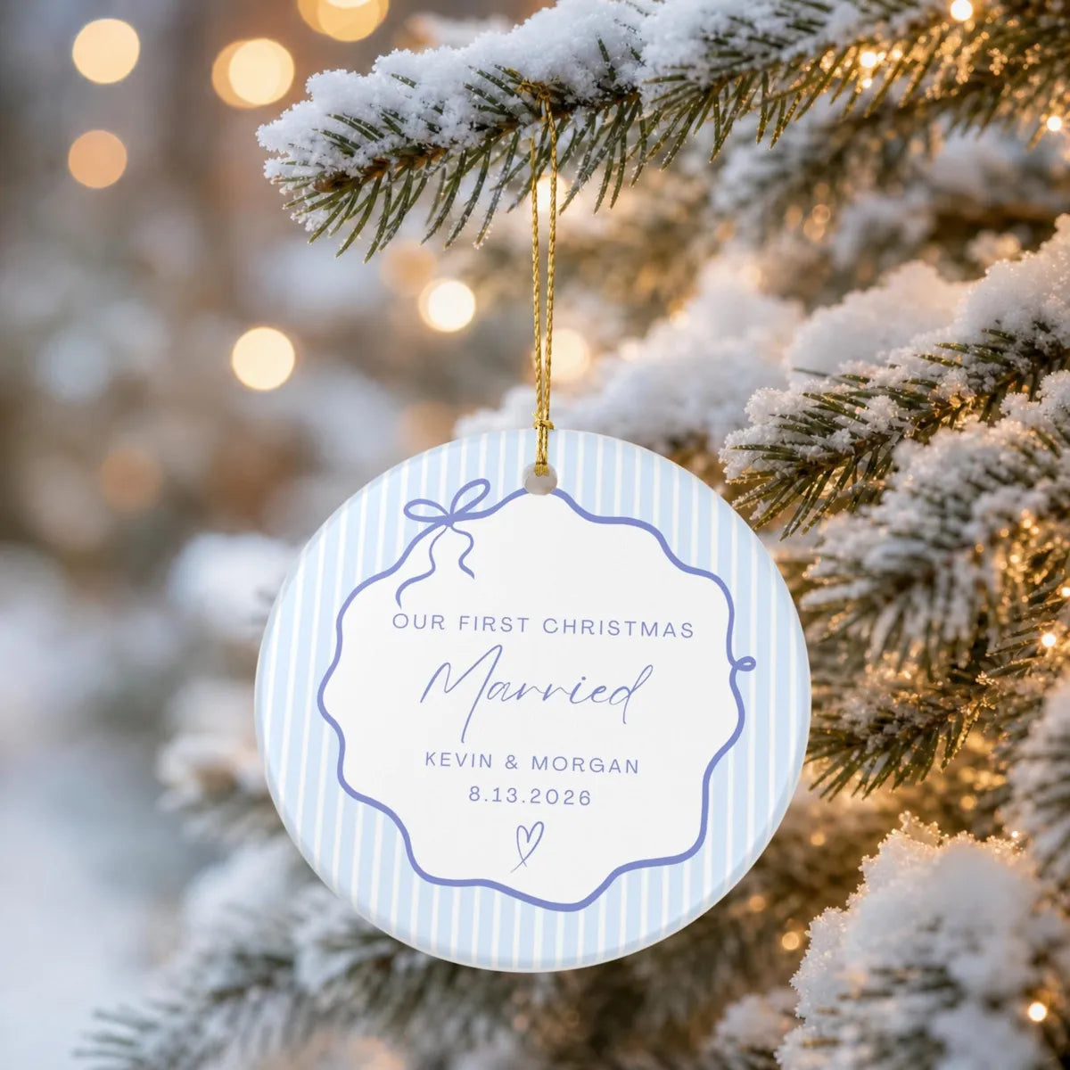 Light blue pinstripe round ceramic First Christmas Married ornament hanging from a snow-covered evergreen branch
