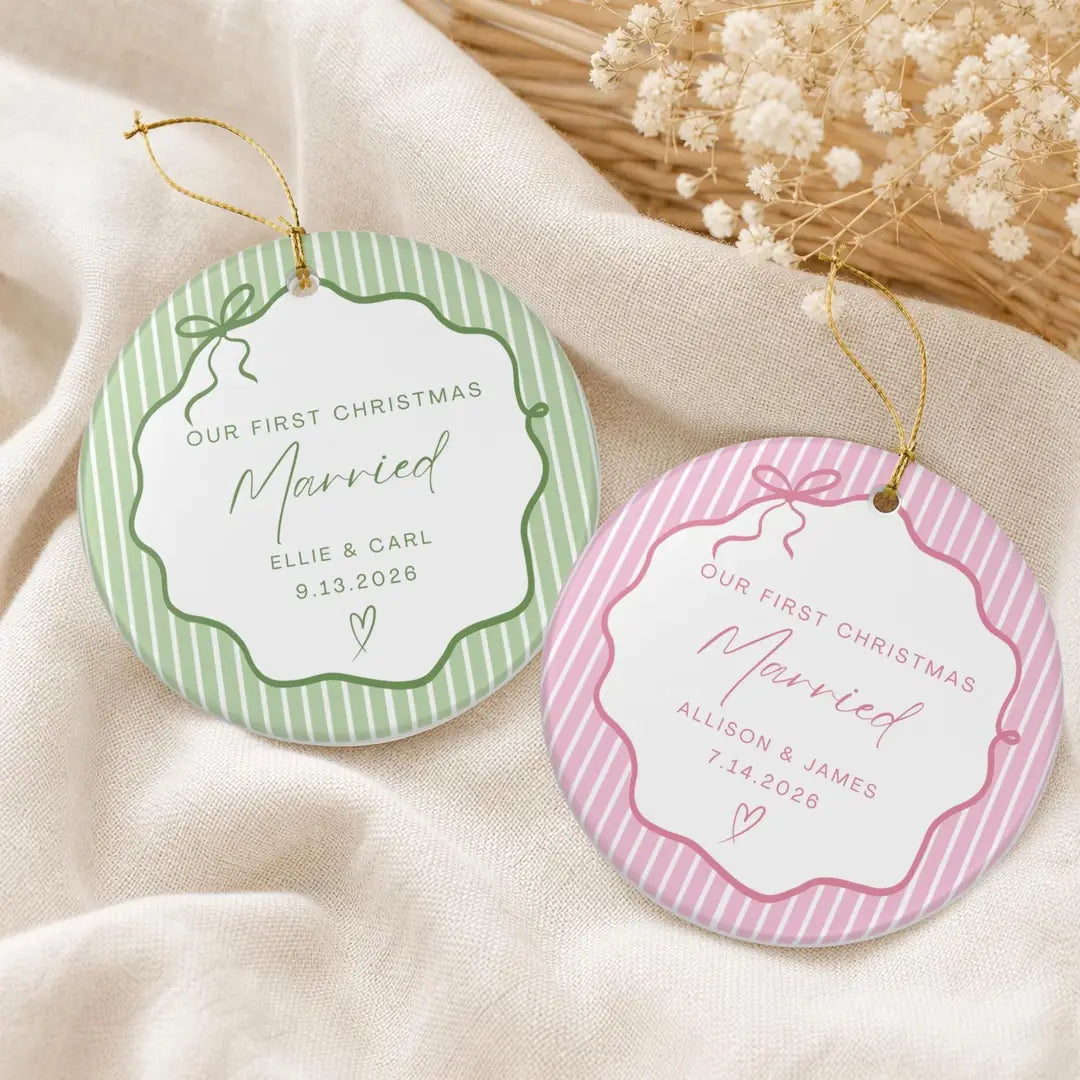 Green and pink pinstripe round ceramic First Christmas Married ornaments with personalized names and date on cream fabric beside dried flowers
