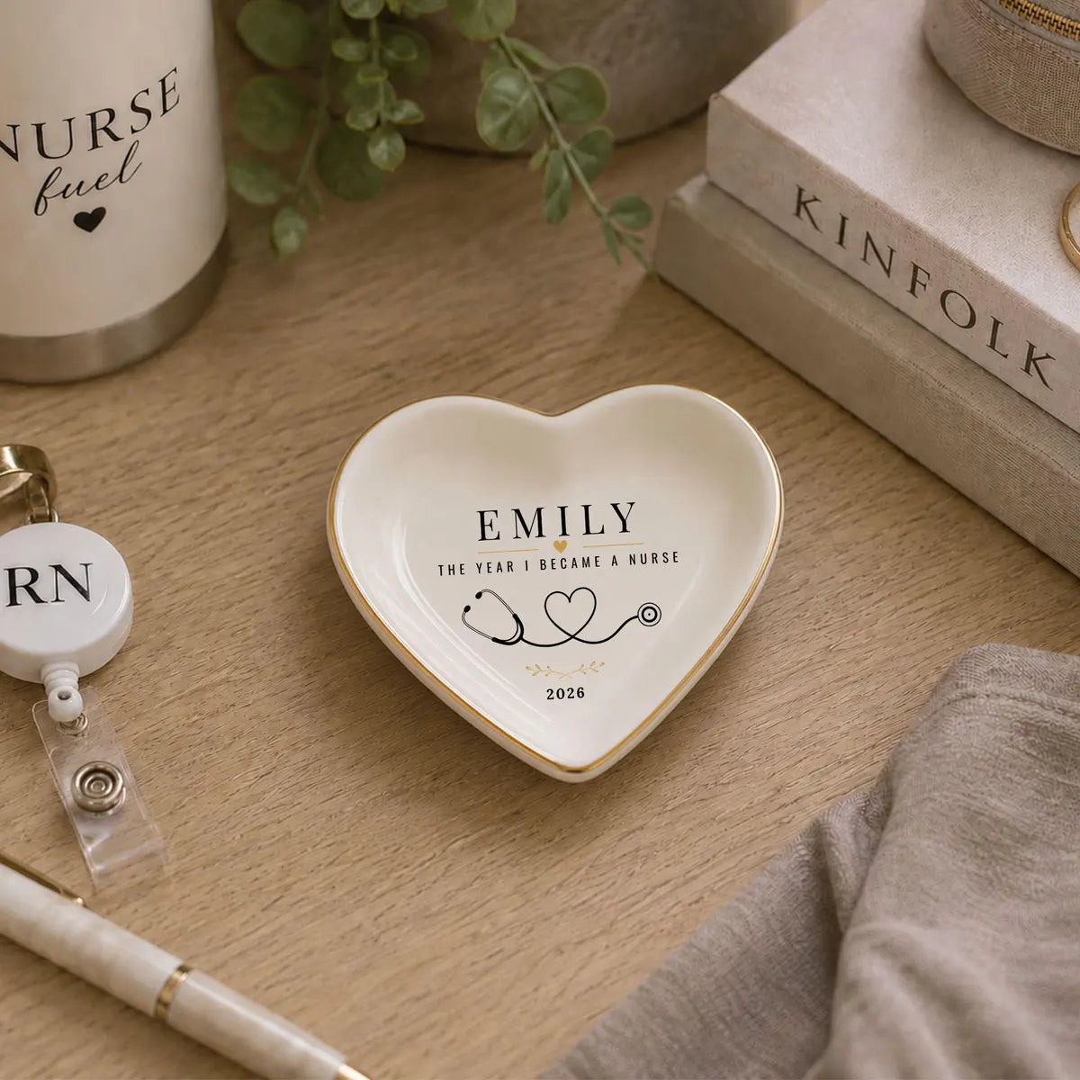 Heart-shaped ceramic nurse ring dish with a name and year on a desk with an RN badge reel and a pen