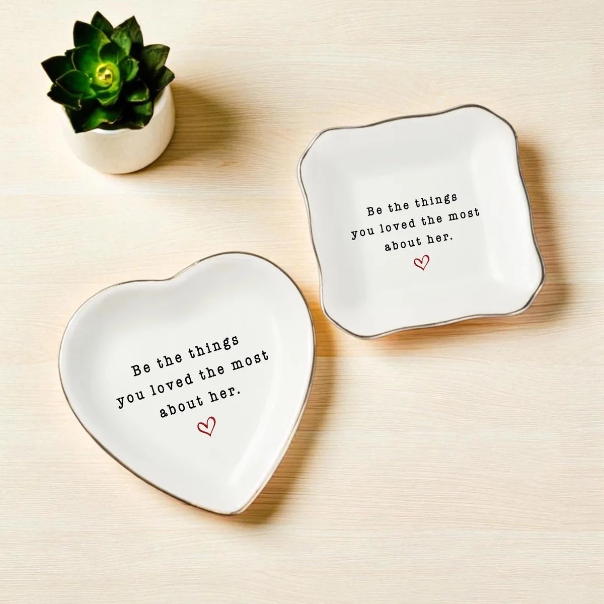 Heart-shaped and square ceramic memorial ring dishes on a wood surface beside a small succulent