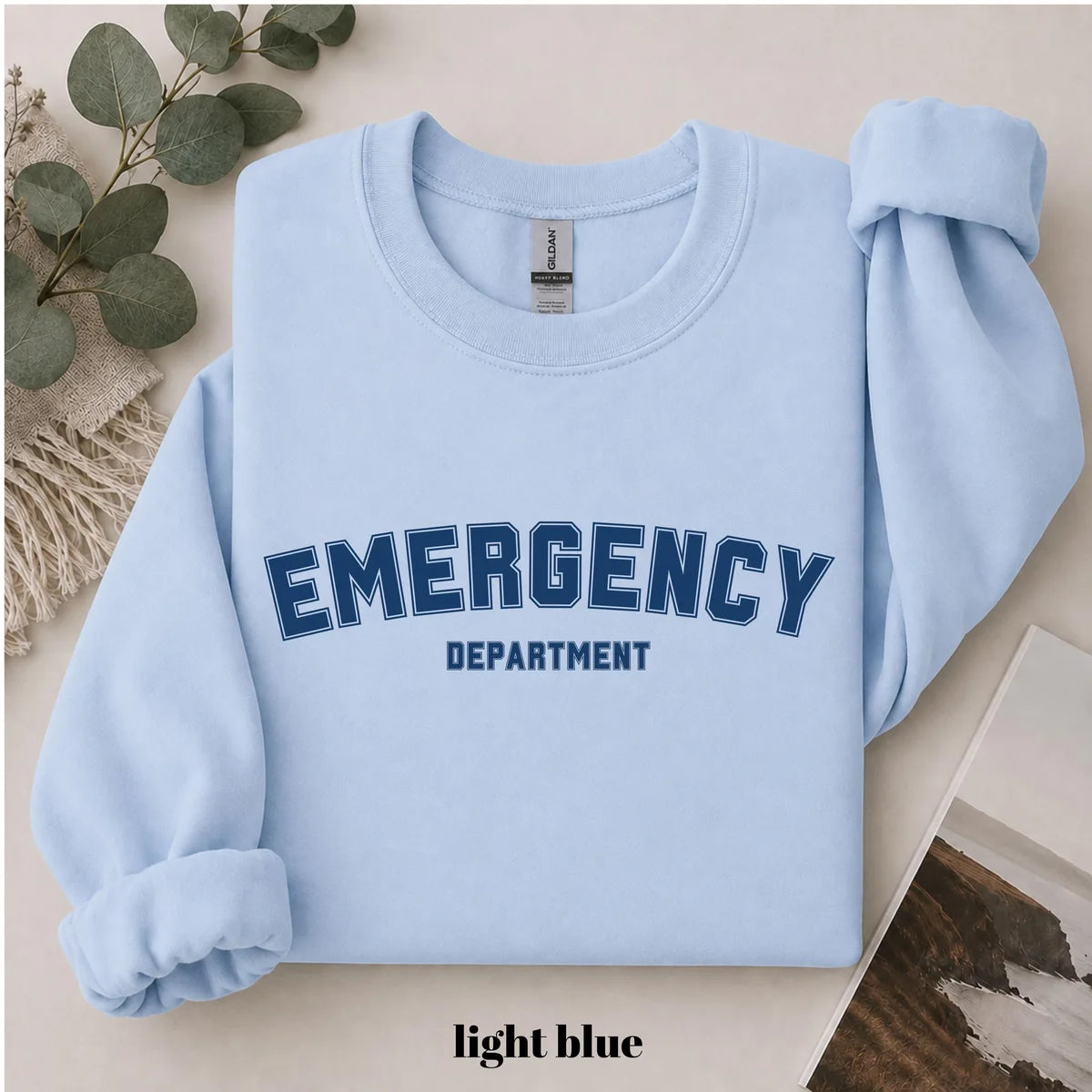 Light Blue crewneck sweatshirt with printed varsity style emergency department lettering, flat lay view.