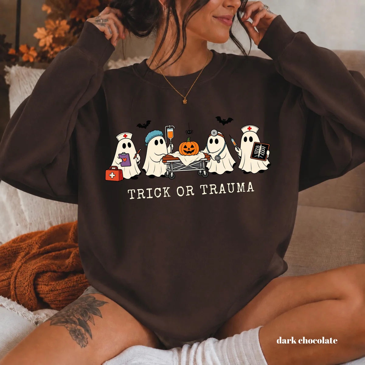 Dark Chocolate crewneck sweatshirt with printed nurse ghosts with a pumpkin and the words trick or trauma, worn by a model.