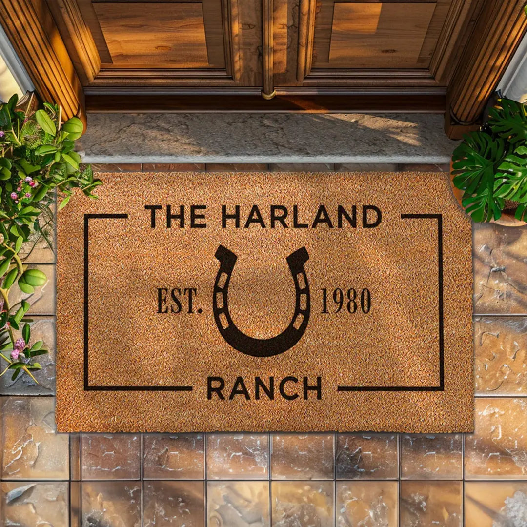 Rectangular coir doormat with a horseshoe ranch design, family name, and established year in front of a wooden door
