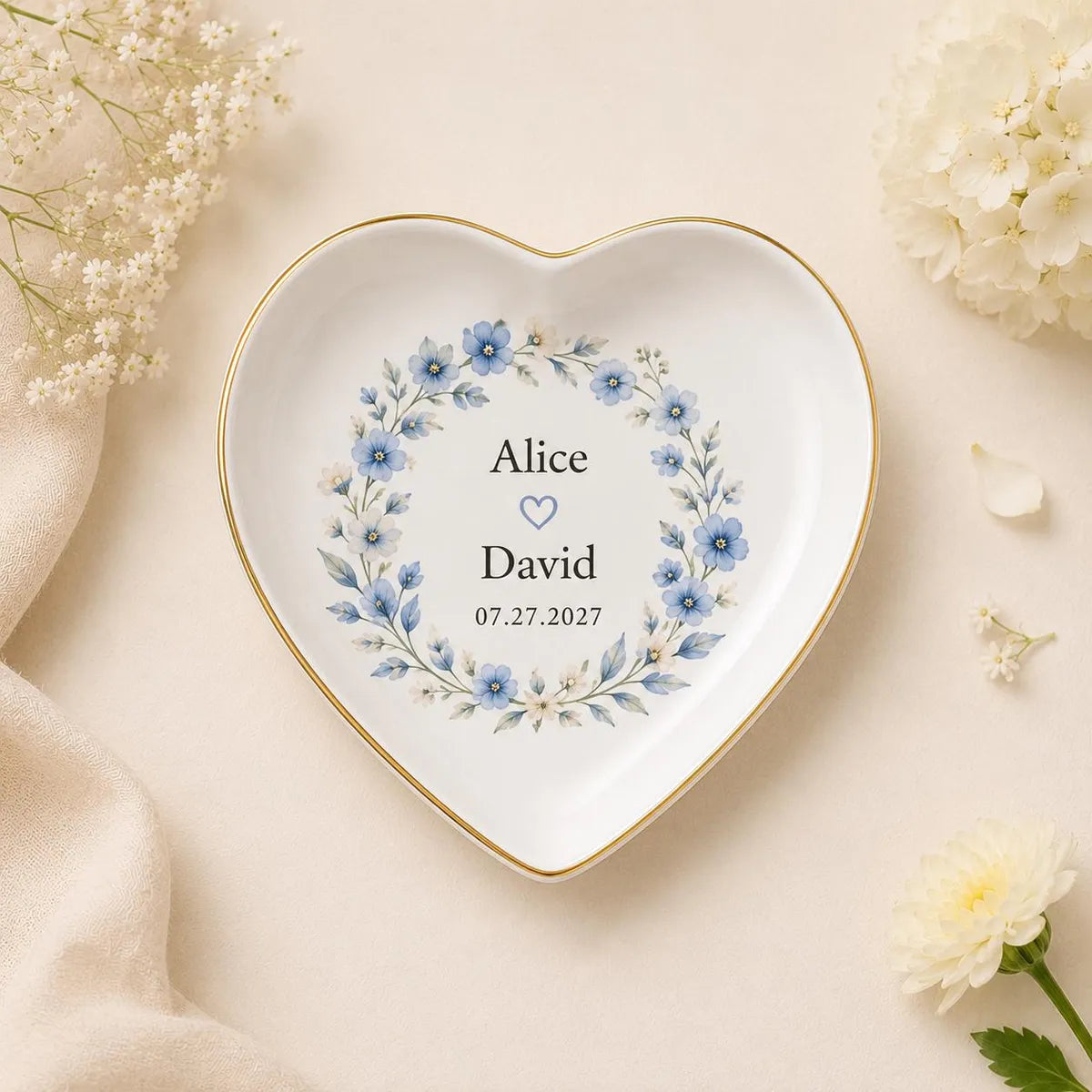 Heart-shaped ceramic wedding ring dish with gold rim and a blue floral wreath around custom names and date