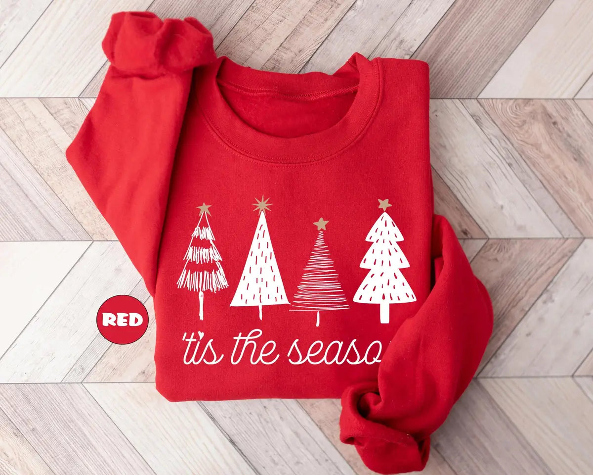 Red GD crewneck sweatshirt with four sketch-style Christmas trees above the script words tis the season, flat lay view.