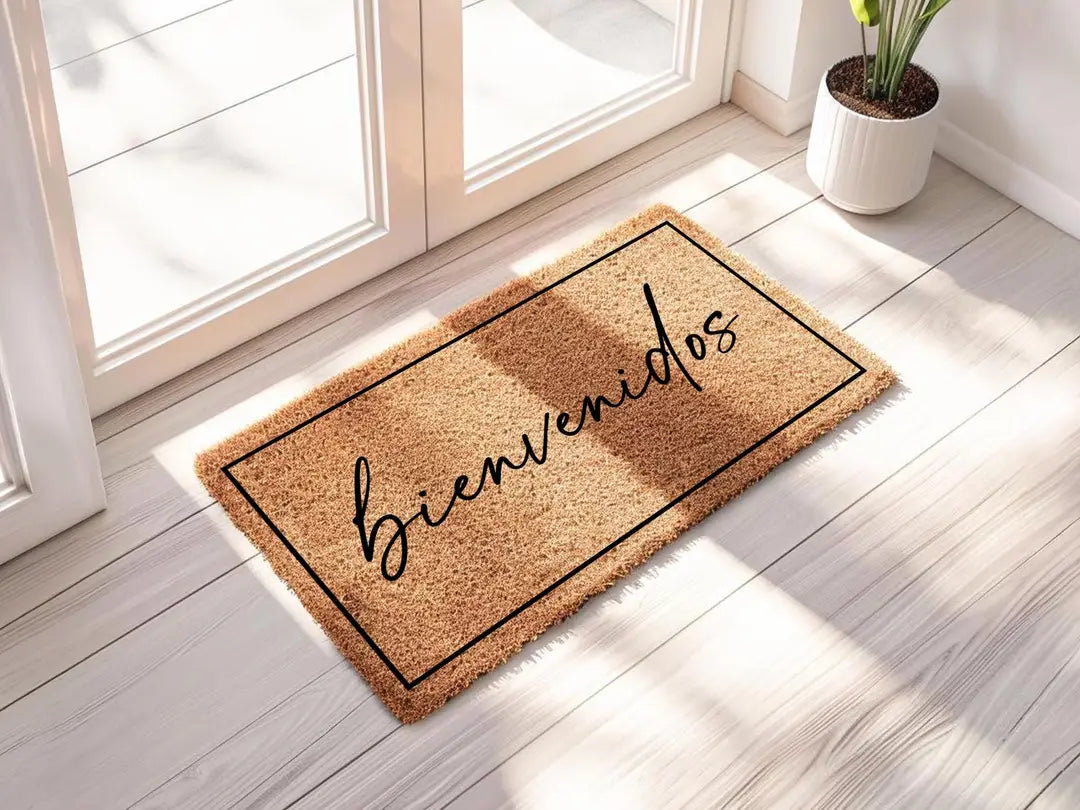 Coir doormat with a framed bienvenidos script message in sunlight beside a glass door and a potted plant