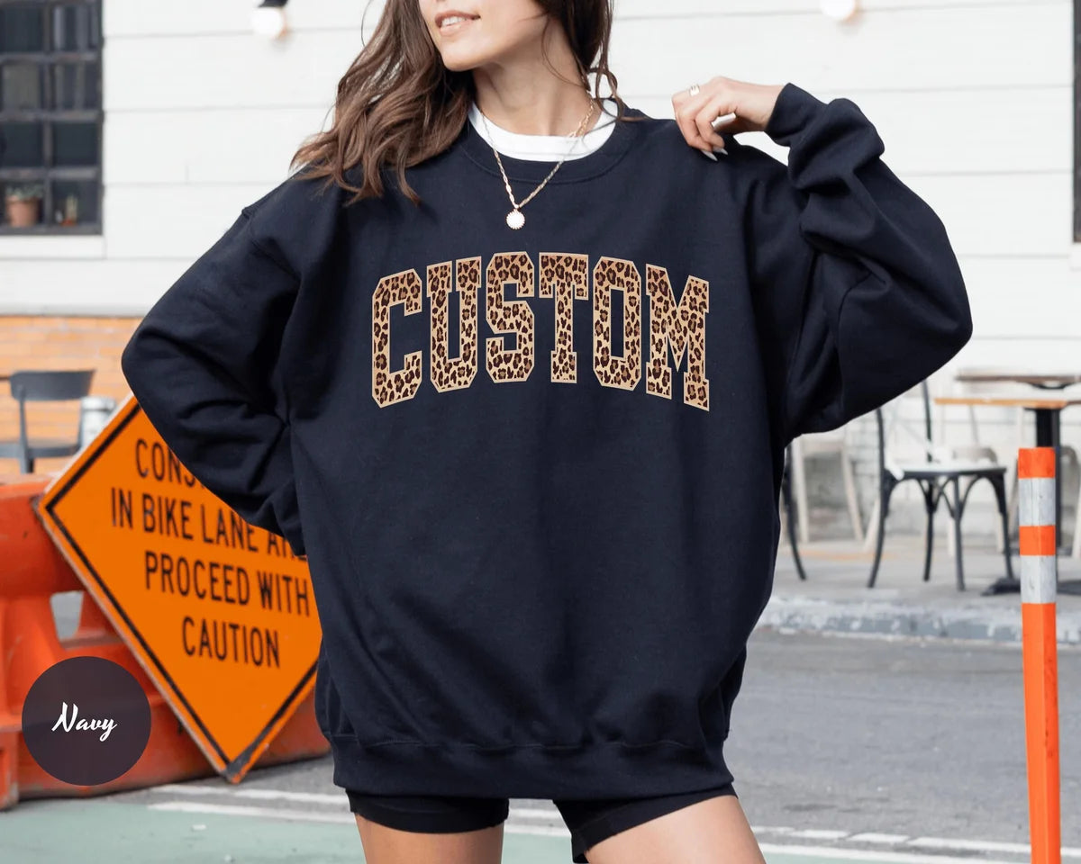 Navy crewneck sweatshirt with bold leopard print varsity lettering with your own custom name or text, worn by a model.