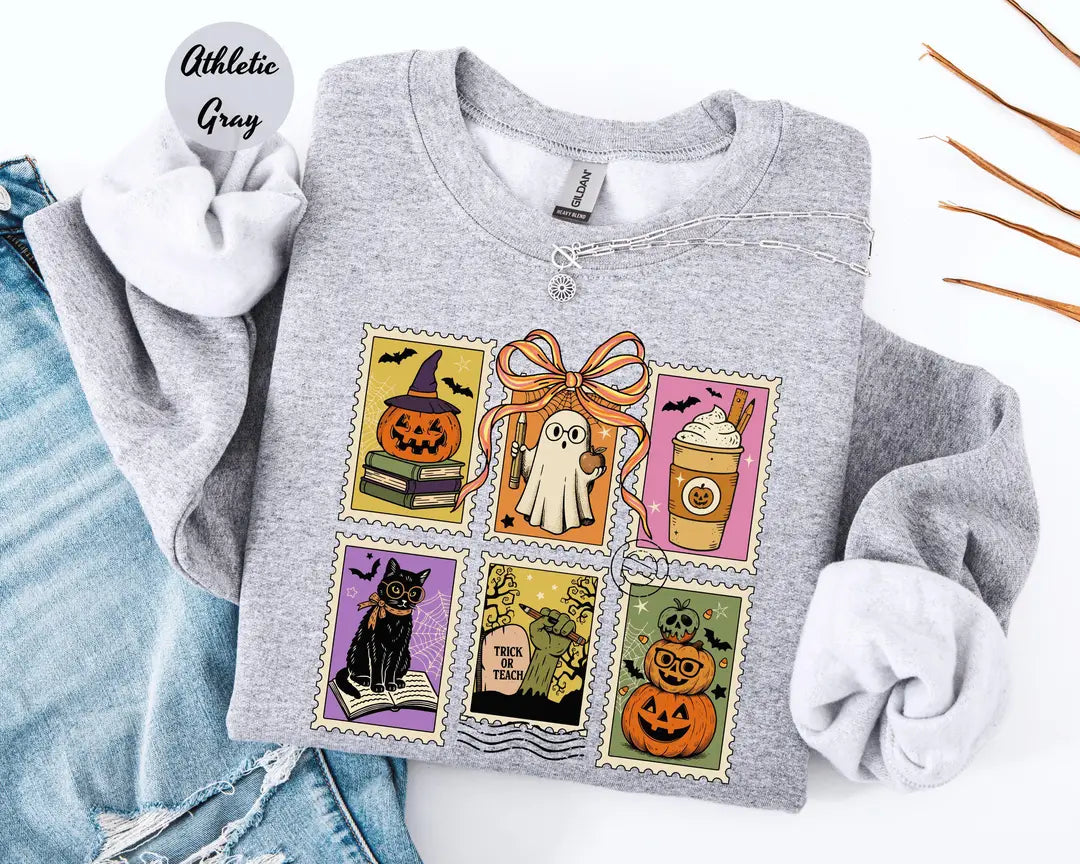Athletic Gray crewneck sweatshirt with six vintage postage-style stamps with a ghost, black cat, pumpkins and a coffee cup, flat lay view.