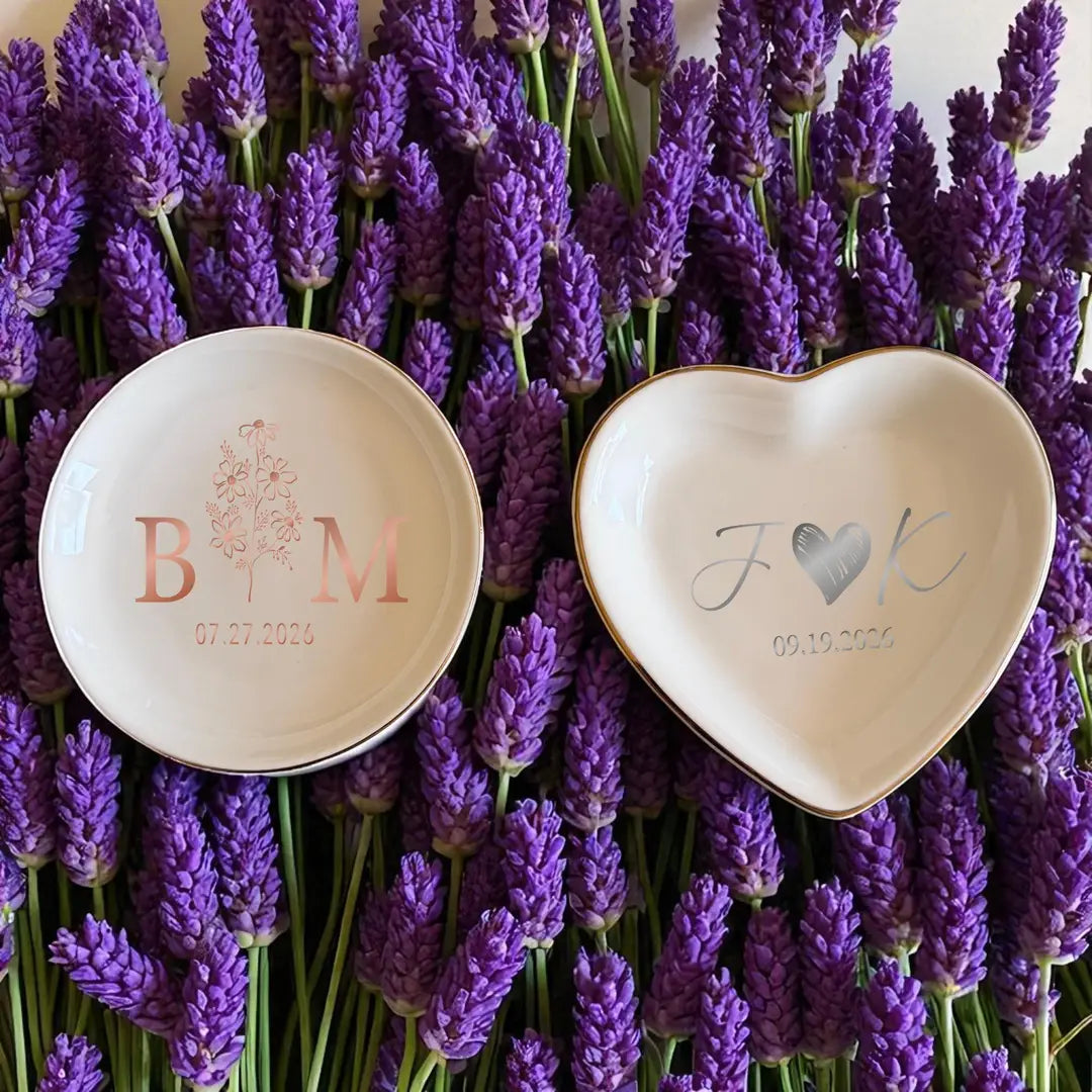 Two ceramic ring dishes in different shapes with rose gold and silver initials and dates, styled with lavender