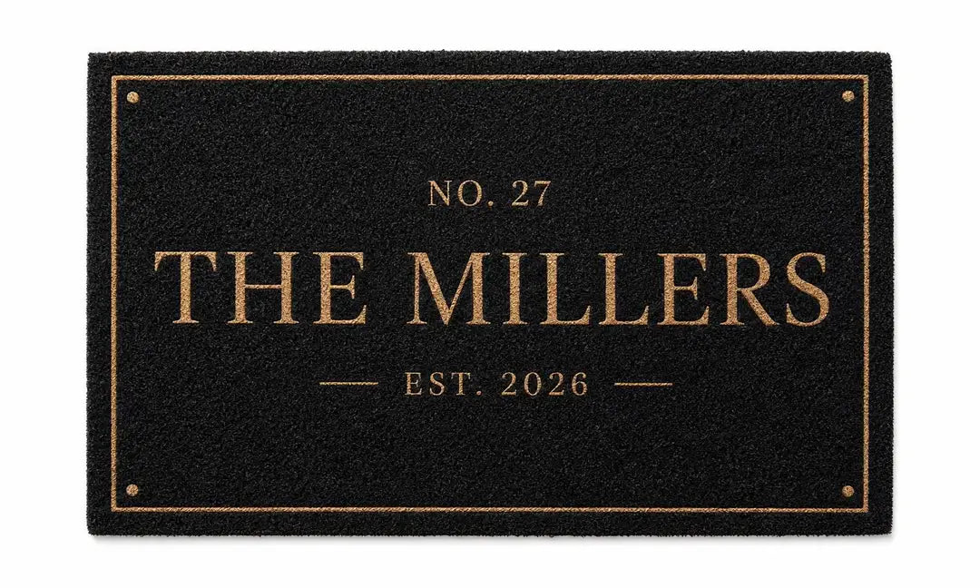Flat view of a black faux coir doormat with a thin gold-tone frame, number line, family name, and established year