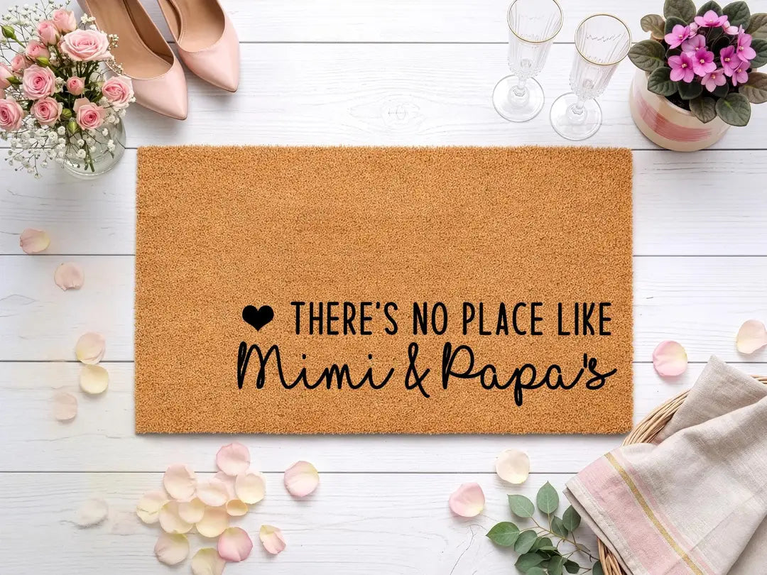 Coir doormat with a There's No Place Like Mimi and Papa's message styled with pink heels, champagne flutes, and rose petals