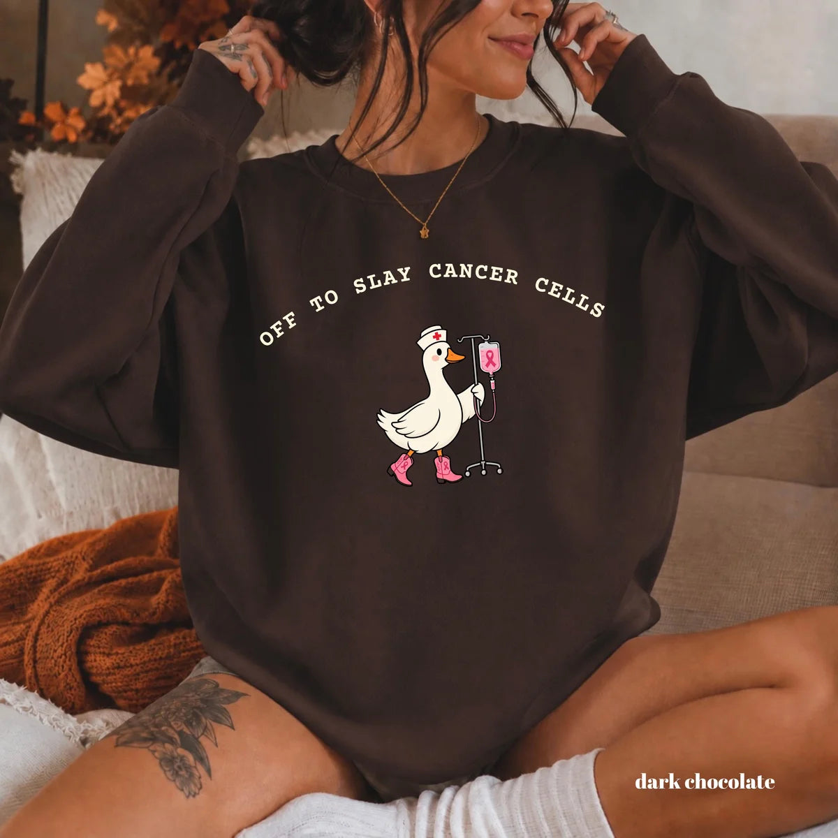 Dark Chocolate crewneck sweatshirt with printed a nurse goose in pink boots with an IV pole and the words off to slay cancer cells, worn by a model.