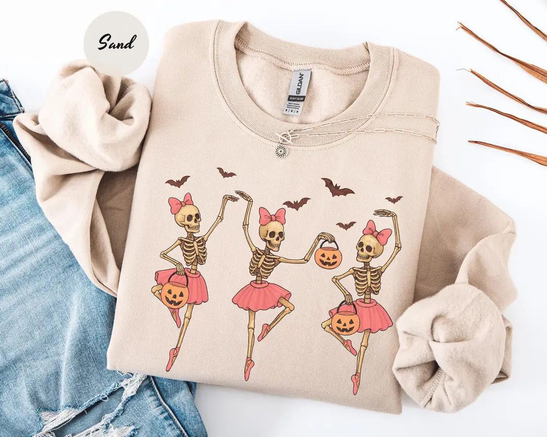 Sand crewneck sweatshirt with printed three ballerina skeletons in pink tutus with pumpkins and bats, flat lay view.