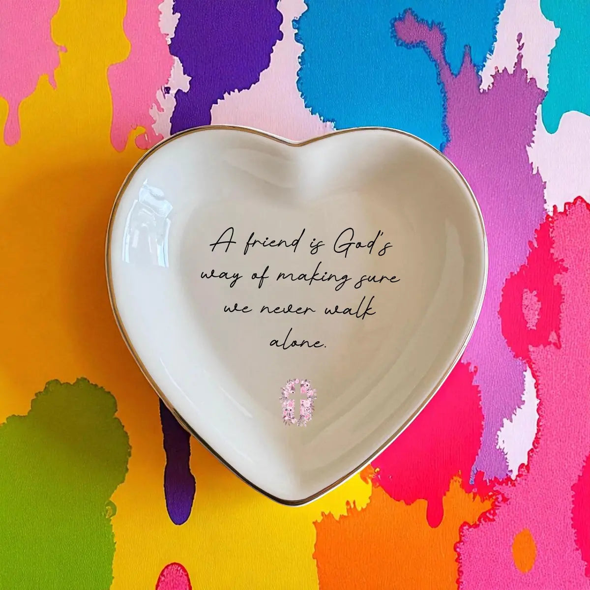 Heart-shaped ceramic friendship ring dish with a floral cross on a colorful painted backdrop