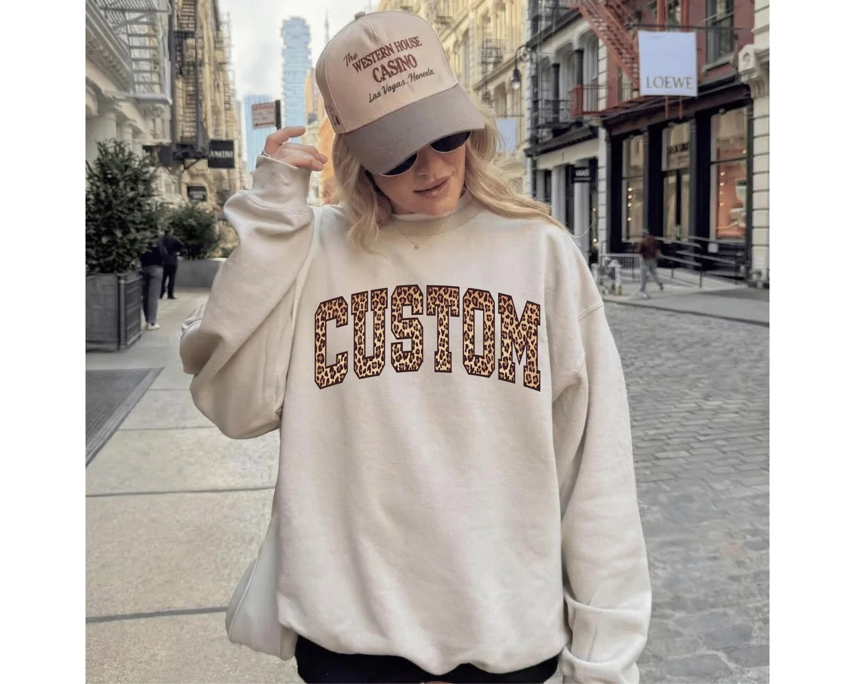 Sand crewneck sweatshirt with bold leopard print varsity lettering with your own custom name or text, worn by a model.