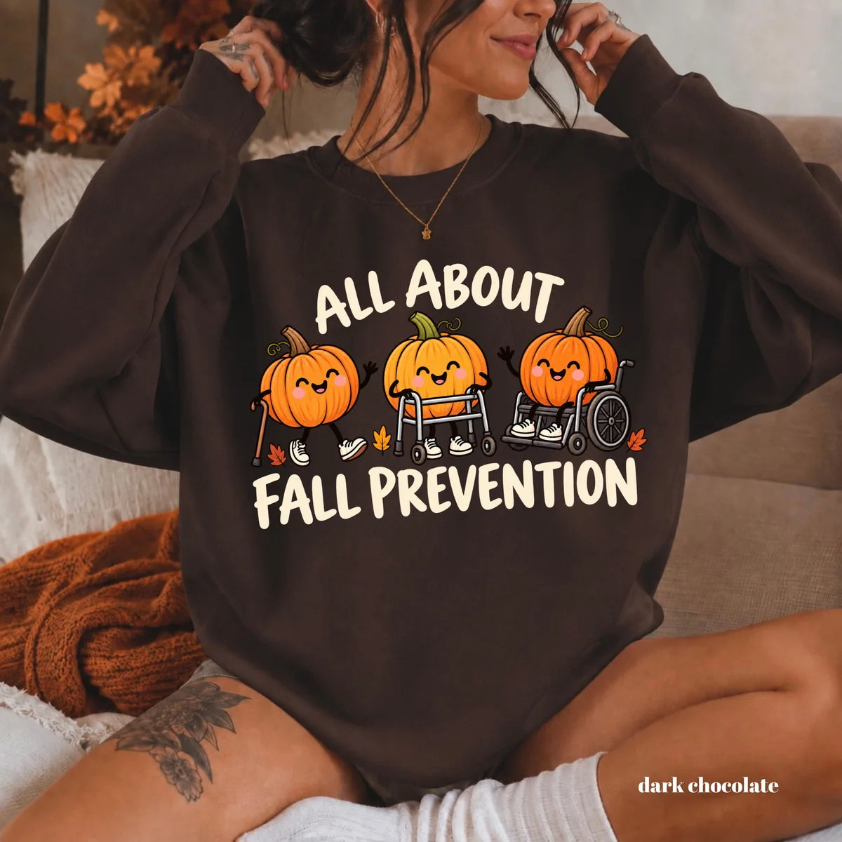 Dark Chocolate crewneck sweatshirt with printed pumpkins with a walker and wheelchair above the words all about fall prevention, worn by a model.
