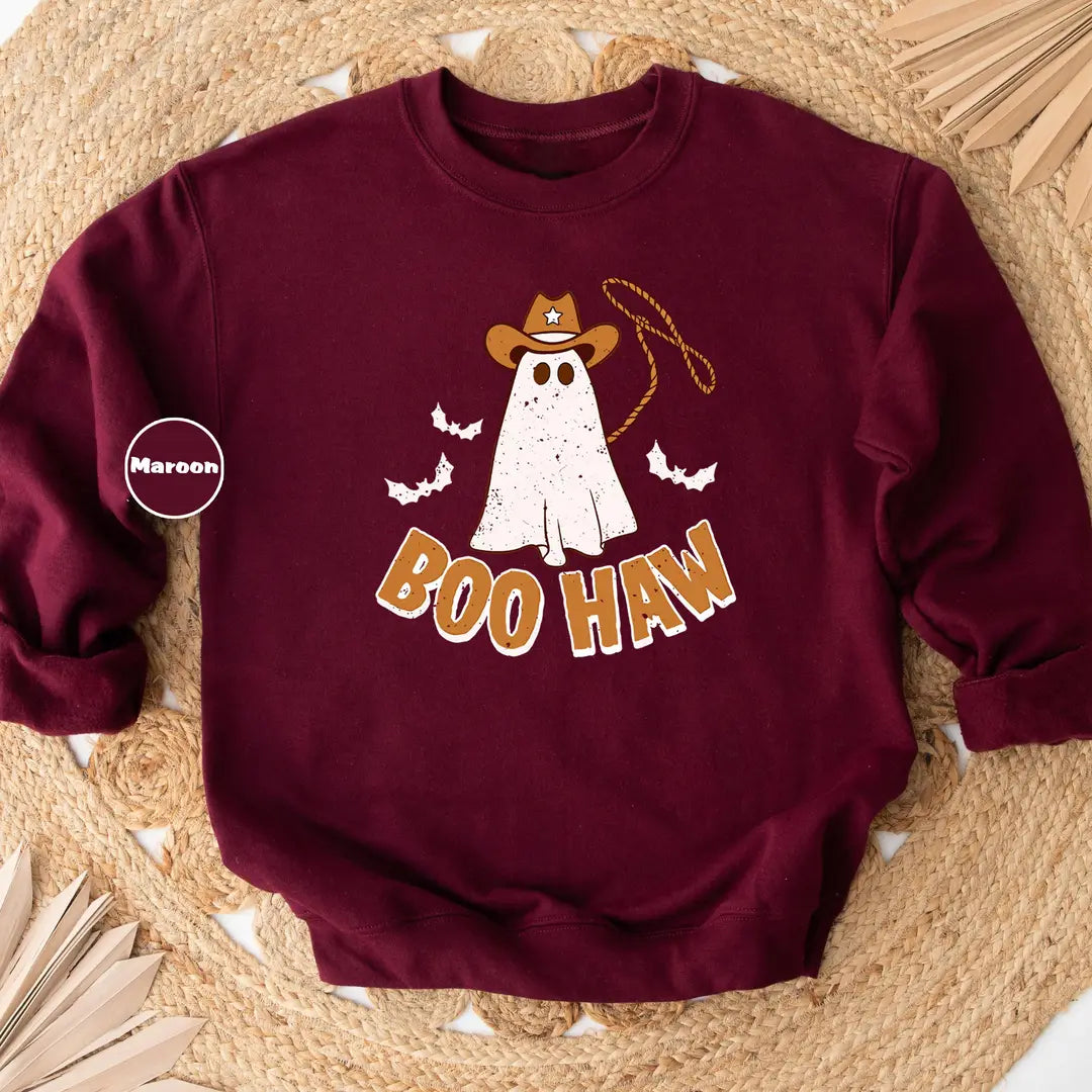 Maroon crewneck sweatshirt with a cowboy ghost with a lasso and bats above the words boo haw, flat lay view.