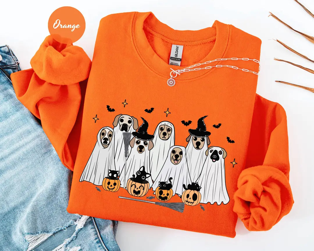 Orange crewneck sweatshirt with printed ghost dogs with witch hats, pumpkins and bats, flat lay view.