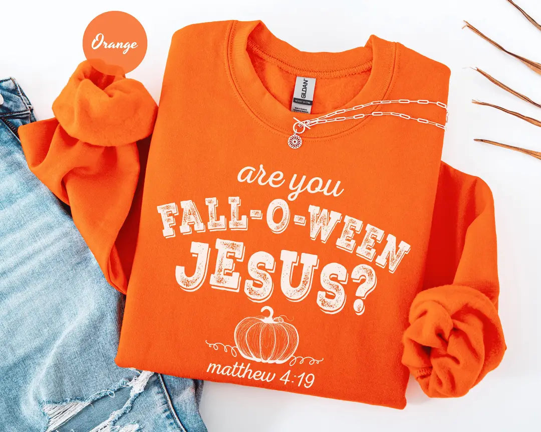 Orange crewneck sweatshirt with printed a pumpkin with the words are you fall-o-ween jesus and matthew 4:19 in a western style font, flat lay view.