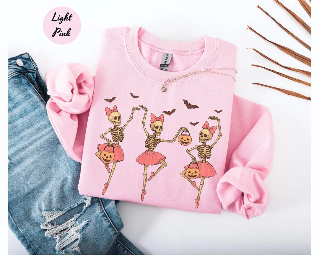 Light Pink crewneck sweatshirt with printed three ballerina skeletons in pink tutus with pumpkins and bats, flat lay view.