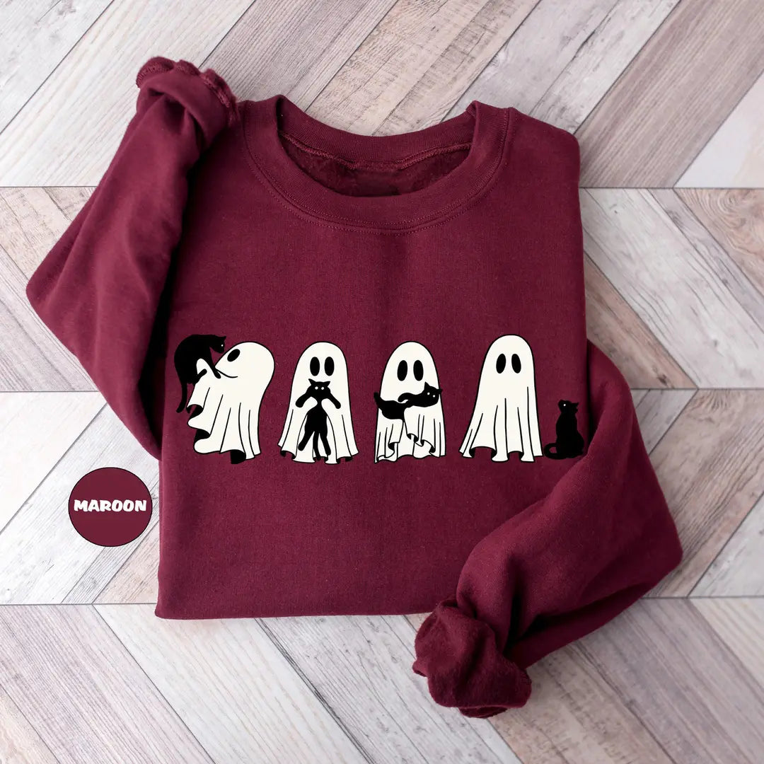 Maroon crewneck sweatshirt with four ghosts and a black cat in a row, flat lay view.