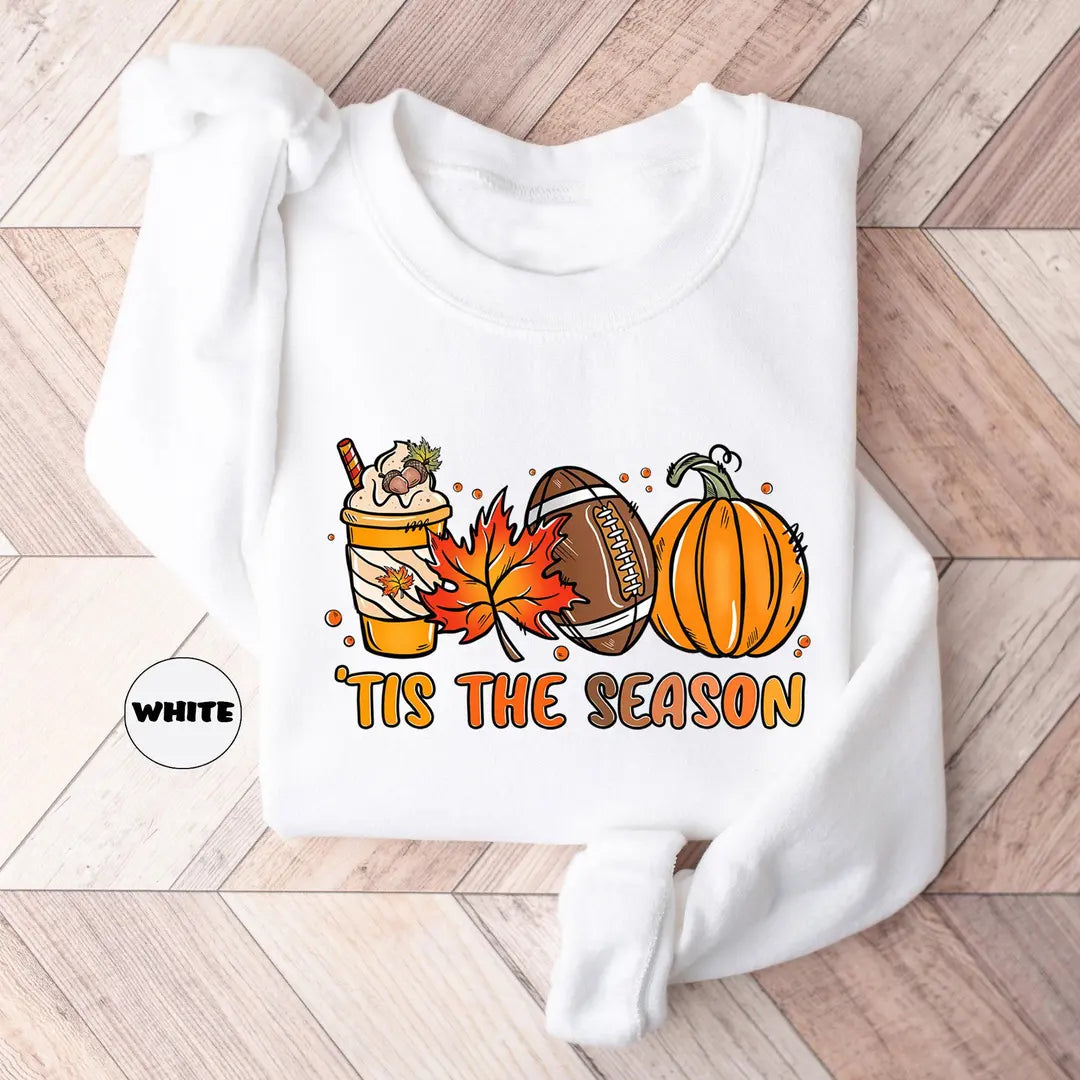White crewneck sweatshirt with a latte, autumn leaves, a football and a pumpkin above the words tis the season, flat lay view.