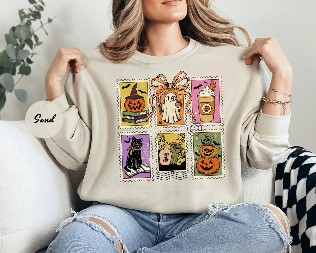 Sand crewneck sweatshirt with six vintage postage-style stamps with a ghost, black cat, pumpkins and a coffee cup, worn by a model.
