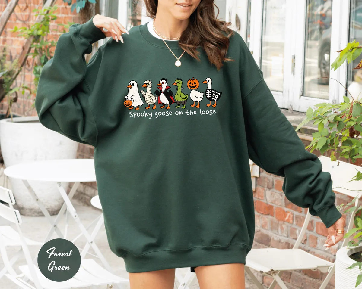 Forest Green crewneck sweatshirt with costumed geese dressed as a ghost, vampire, pumpkin and skeleton above the words spooky goose on the loose, worn by a model.