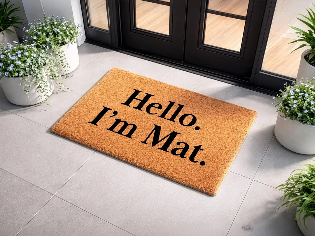 Coir doormat with a Hello I'm Mat message at black double doors with white flower pots