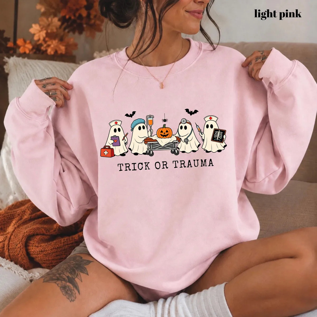 Light Pink crewneck sweatshirt with printed nurse ghosts with a pumpkin and the words trick or trauma, worn by a model.