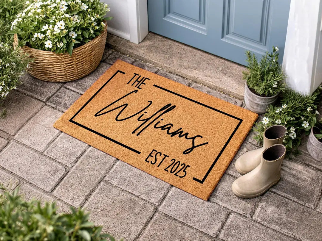 Coir doormat with a framed family name and established year on brick pavers beside a light blue door with rain boots