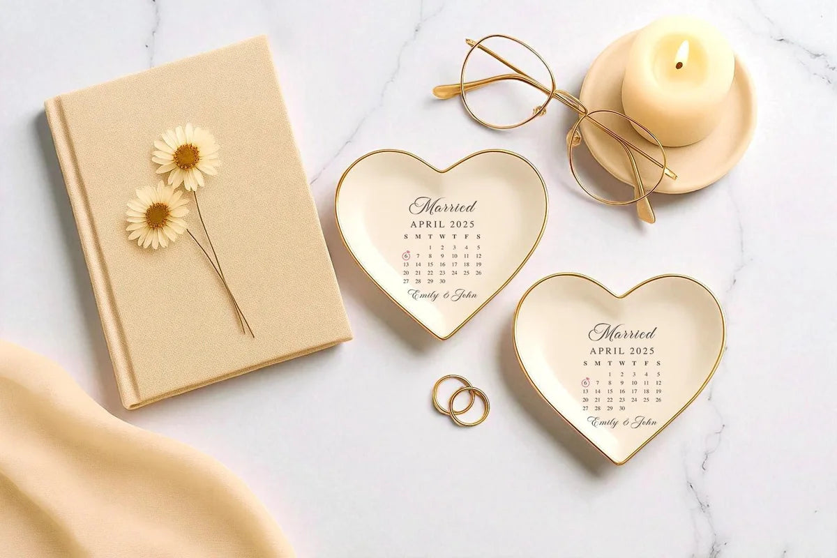 Two heart-shaped ceramic Married calendar ring dishes styled with a linen book, candle, glasses, and gold rings