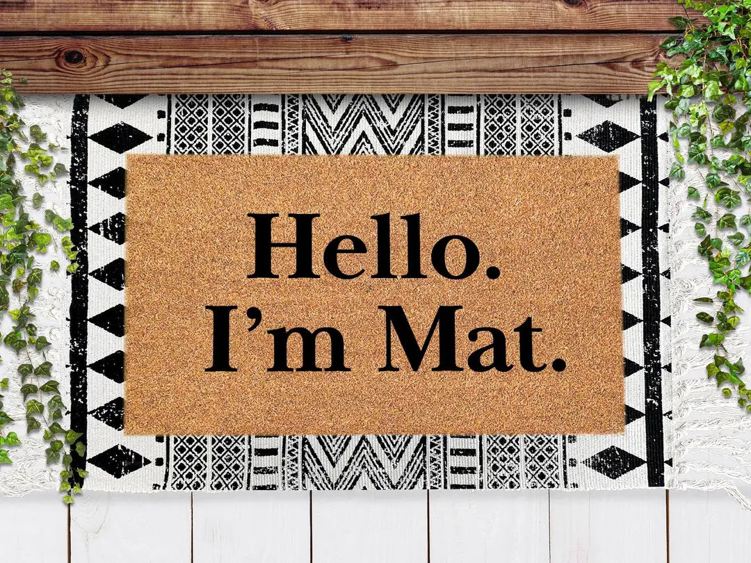 Coir doormat with a Hello I'm Mat message layered on a black and white geometric rug under a wooden beam