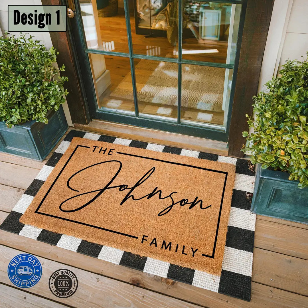 Coir doormat with a framed script family name layered on a black and white check rug at a glass front door with boxwood planters