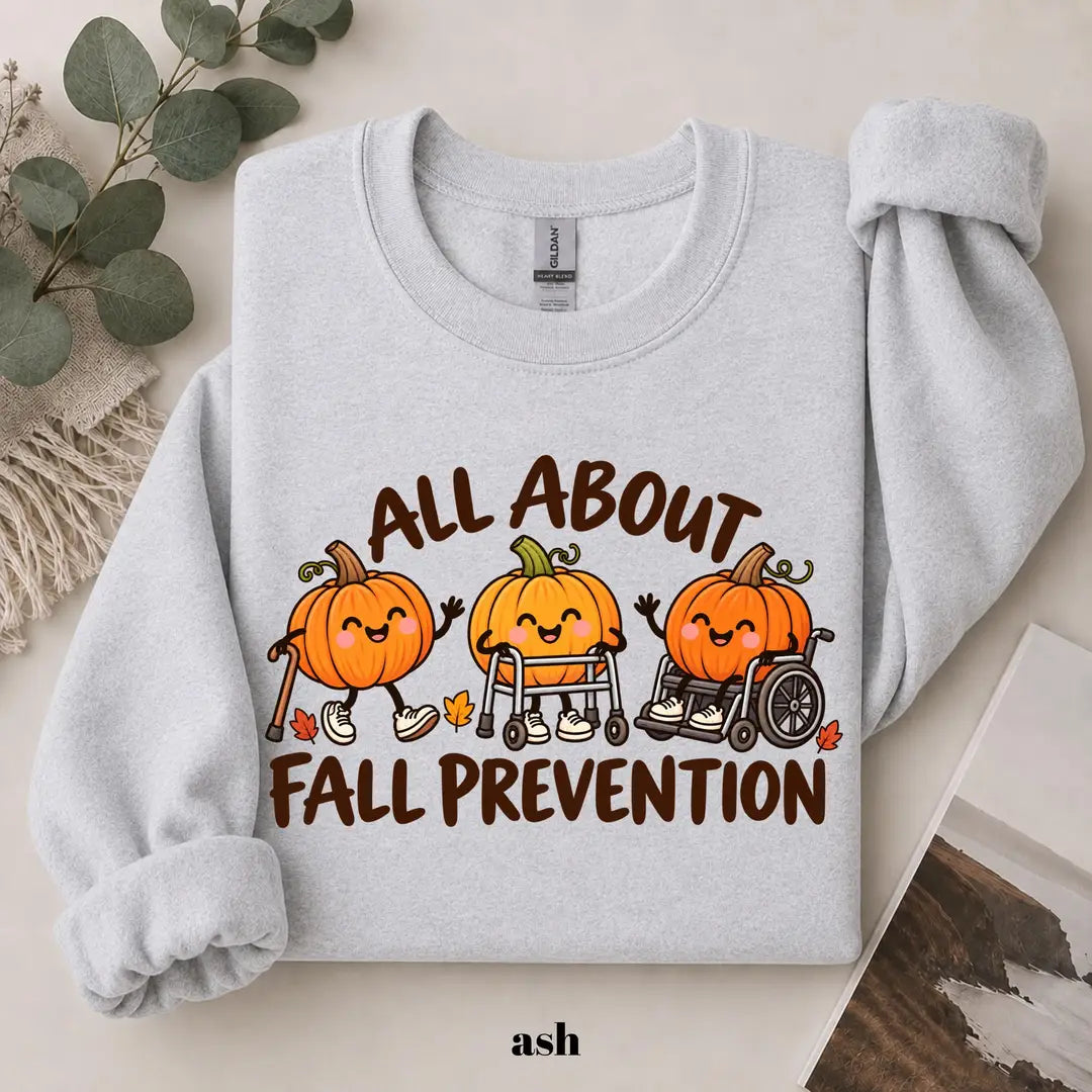 Ash crewneck sweatshirt with printed pumpkins with a walker and wheelchair above the words all about fall prevention, flat lay view.
