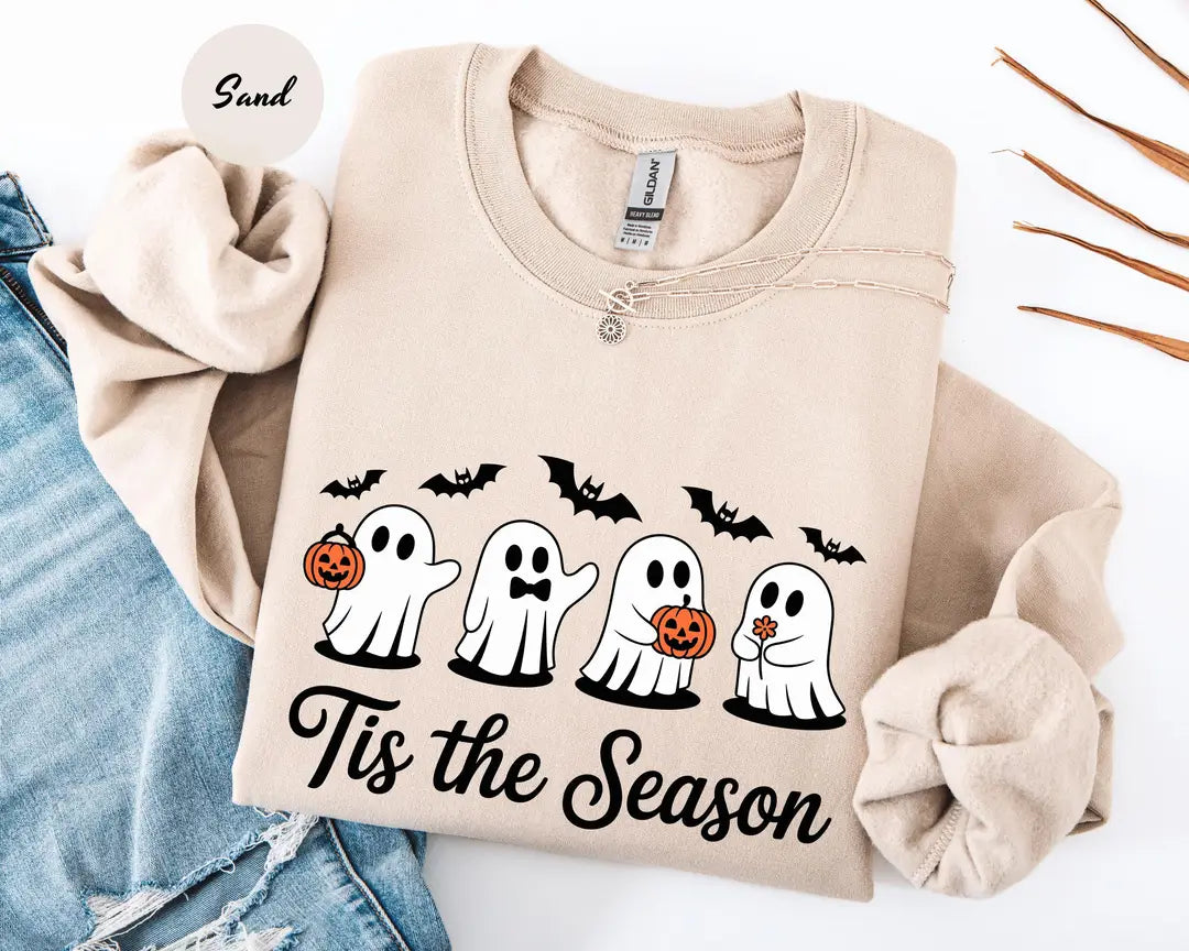 Sand crewneck sweatshirt with printed four cute ghosts with pumpkins and bats above the words tis the season, flat lay view.