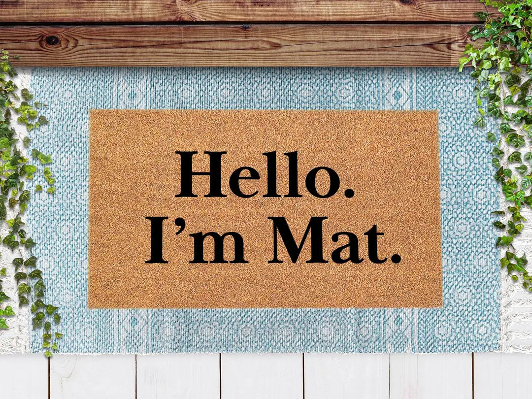 Coir doormat with a Hello I'm Mat message layered on a light blue patterned rug under a wooden beam