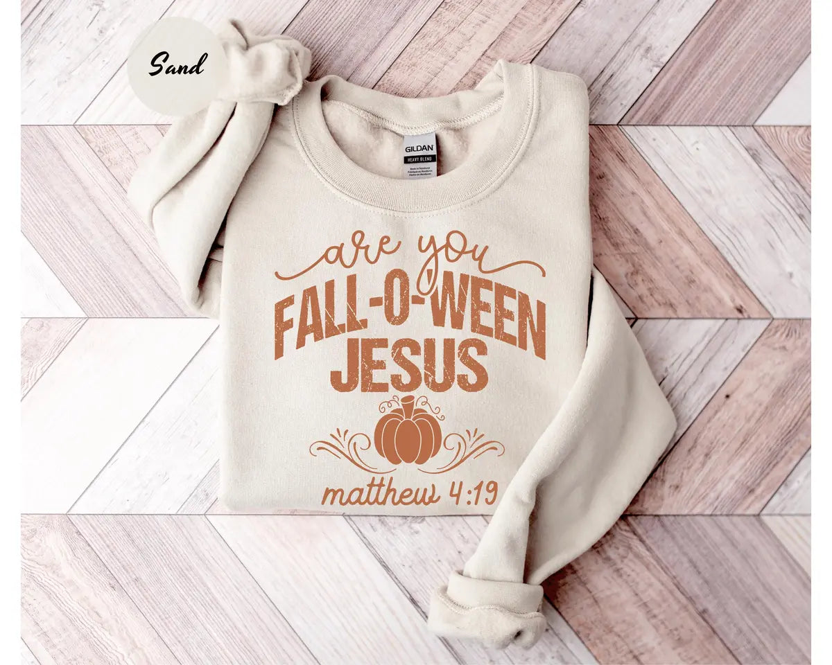 Sand crewneck sweatshirt with printed a pumpkin with the words are you fall-o-ween jesus and matthew 4:19, flat lay view.