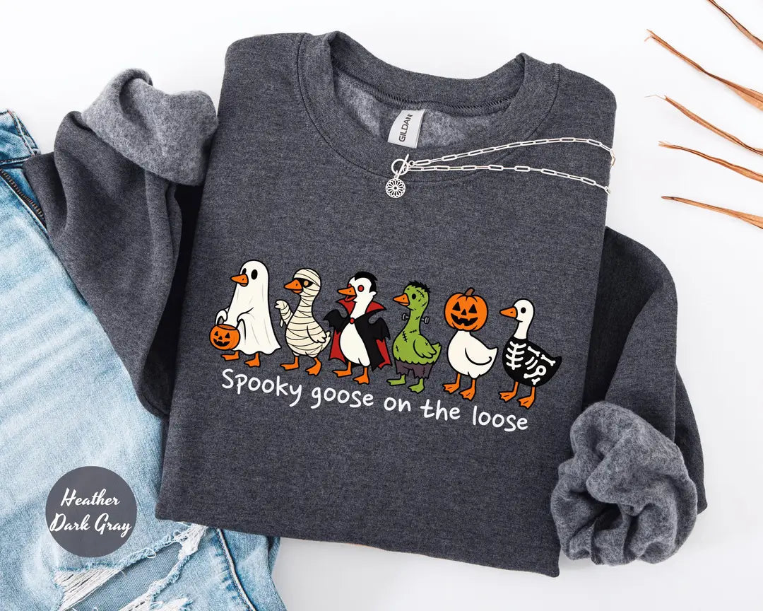 Heather Dark Gray crewneck sweatshirt with costumed geese dressed as a ghost, vampire, pumpkin and skeleton above the words spooky goose on the loose, flat lay view.