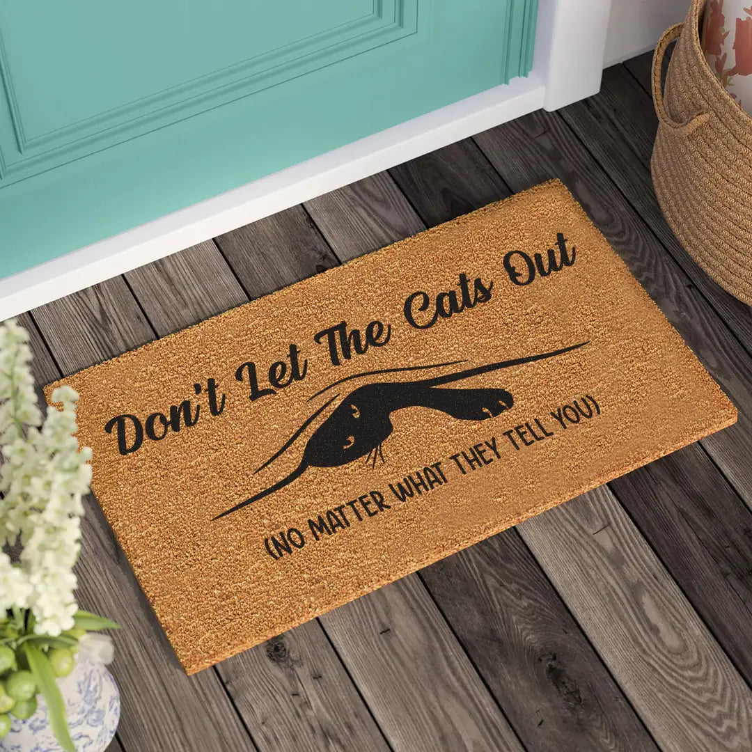 Rectangular coir doormat with a peeking black cat and the message Don't Let The Cats Out in front of a teal door
