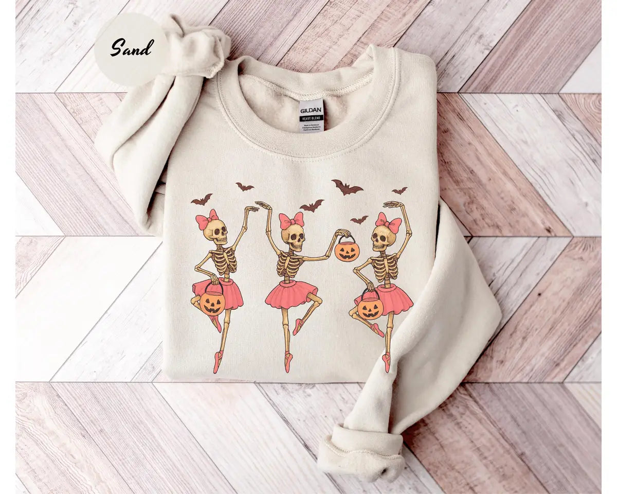 Sand crewneck sweatshirt with printed three ballerina skeletons in pink tutus with pumpkins and bats, flat lay view.