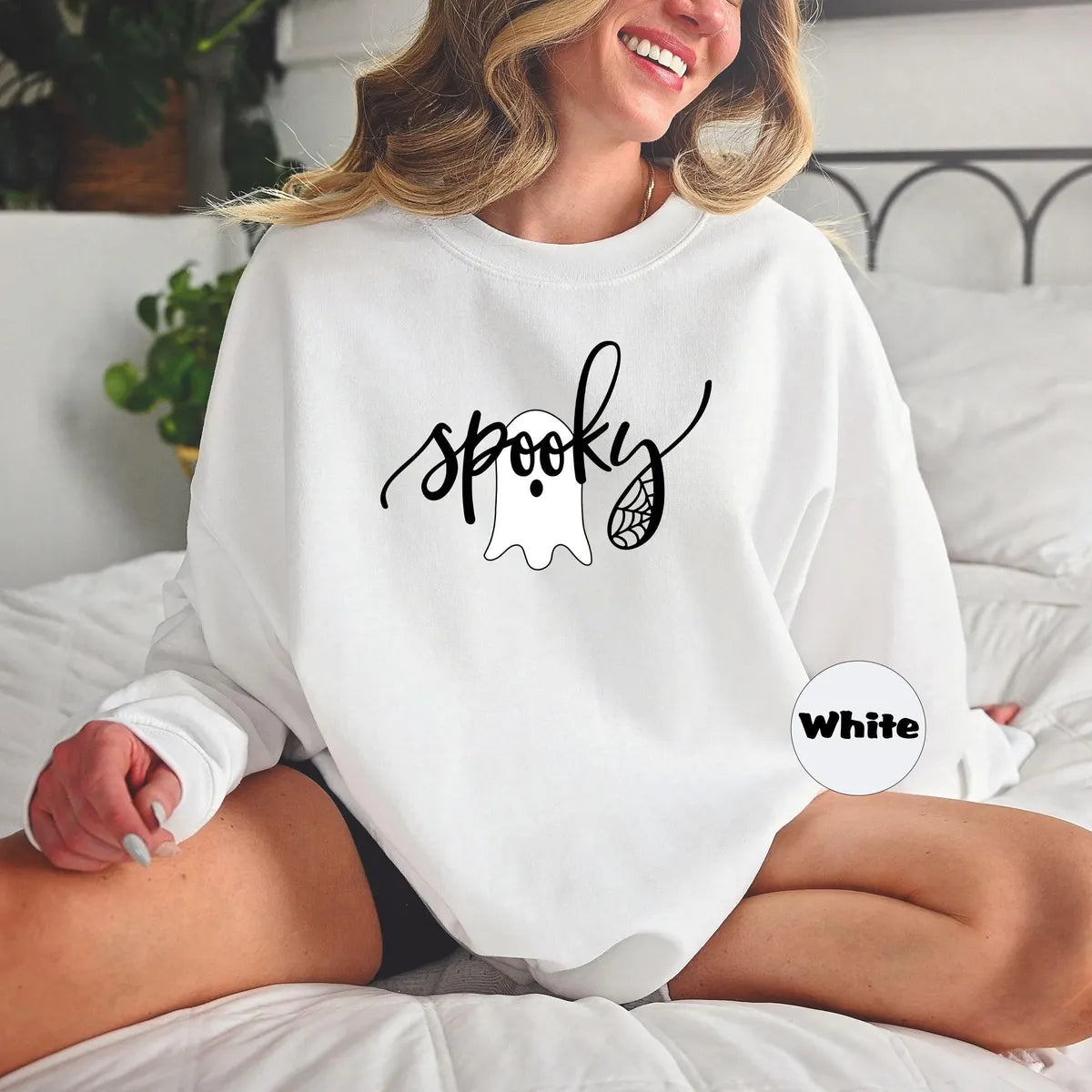 White crewneck sweatshirt with the script word spooky with a ghost and spider web, worn by a model.