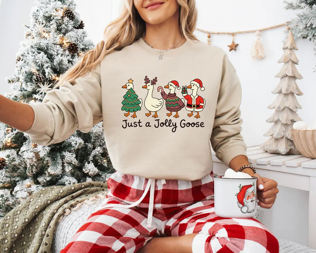 Sand crewneck sweatshirt with geese dressed as a Christmas tree, reindeer and Santa above the words just a jolly goose, worn by a model.