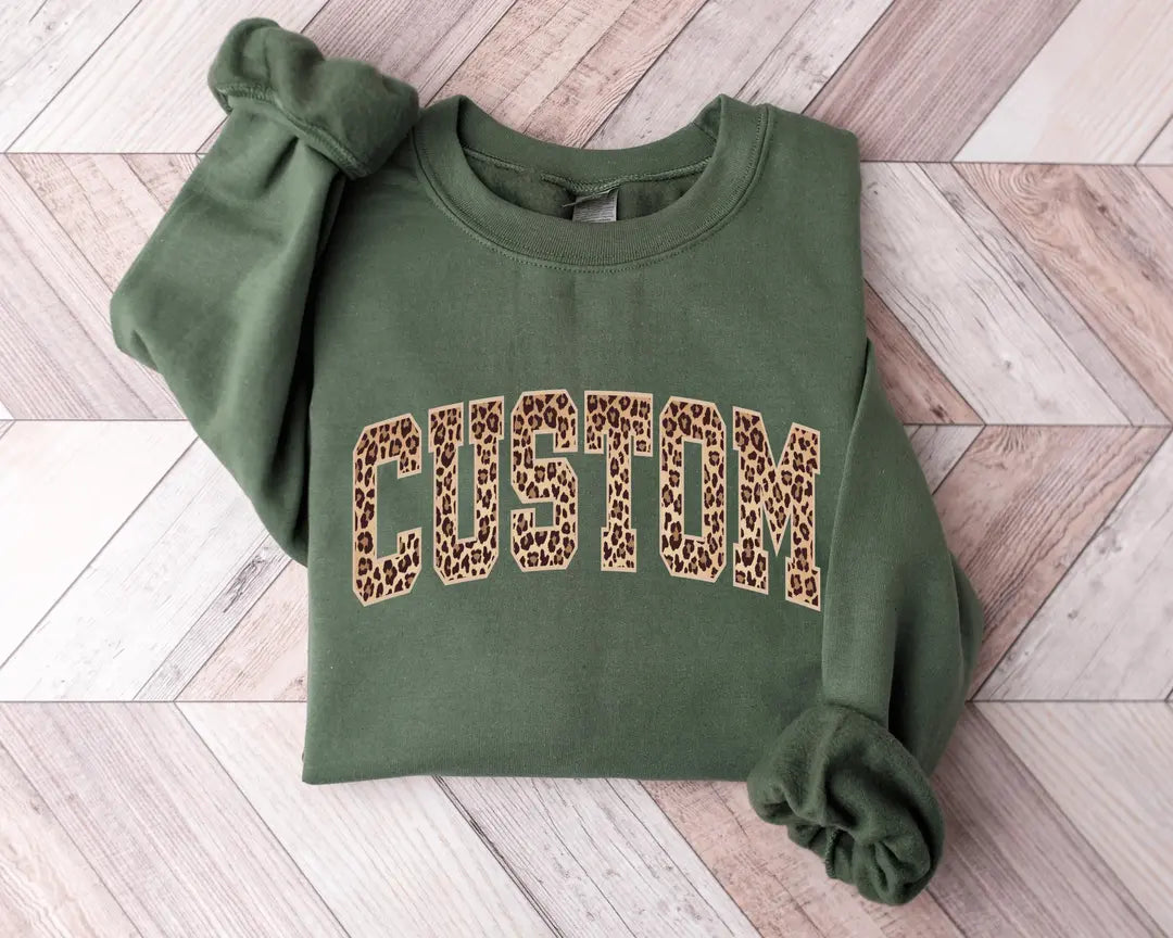 Military Green crewneck sweatshirt with bold leopard print varsity lettering with your own custom name or text, flat lay view.