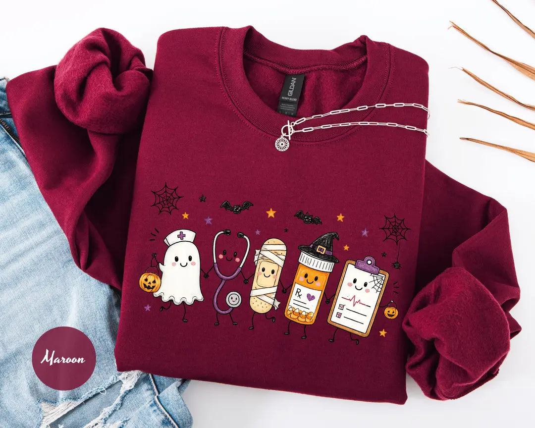 Maroon crewneck sweatshirt with a ghost, stethoscope, bandage and medical chart characters with Halloween details, flat lay view.