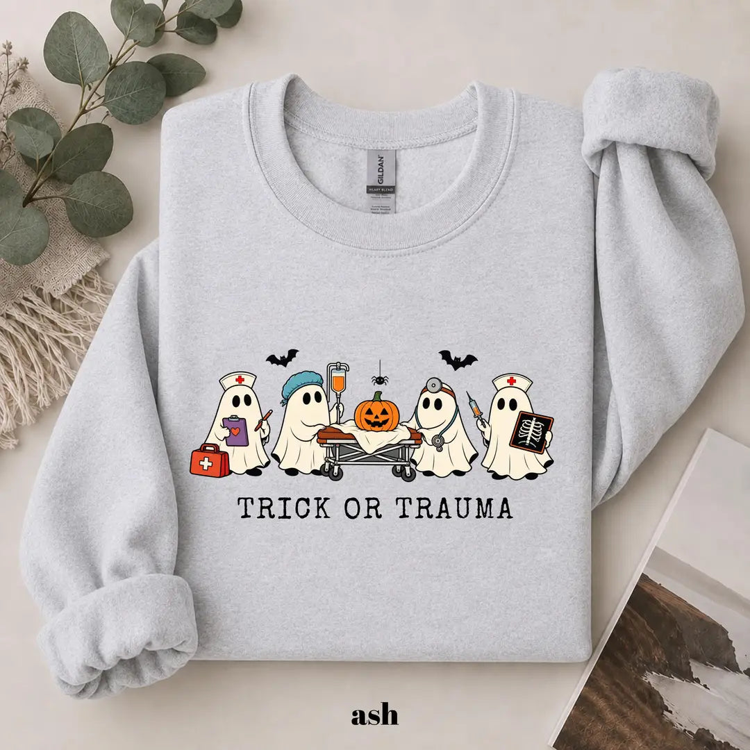 Ash crewneck sweatshirt with printed nurse ghosts with a pumpkin and the words trick or trauma, flat lay view.