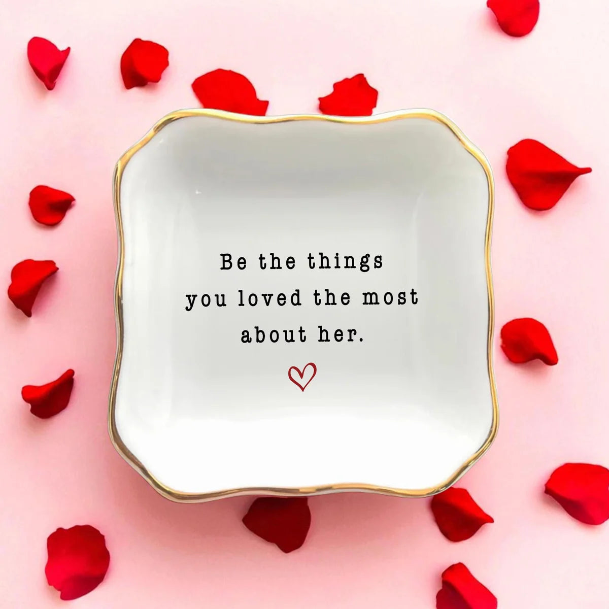 Square ceramic memorial ring dish with scalloped gold rim and a small heart, styled with red rose petals