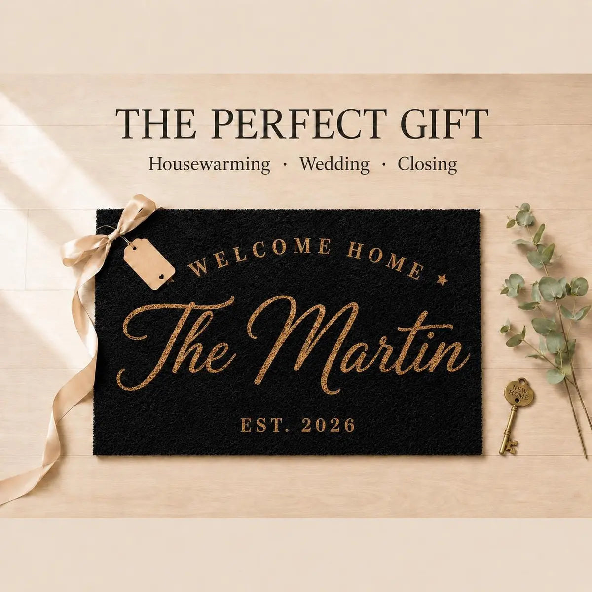 Black doormat with an arched Welcome Home line, script surname, and year styled as a gift with ribbon, tag, and key