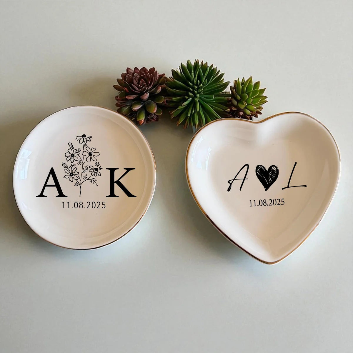 Two ceramic ring dishes in different shapes with black initials and dates, styled with succulents